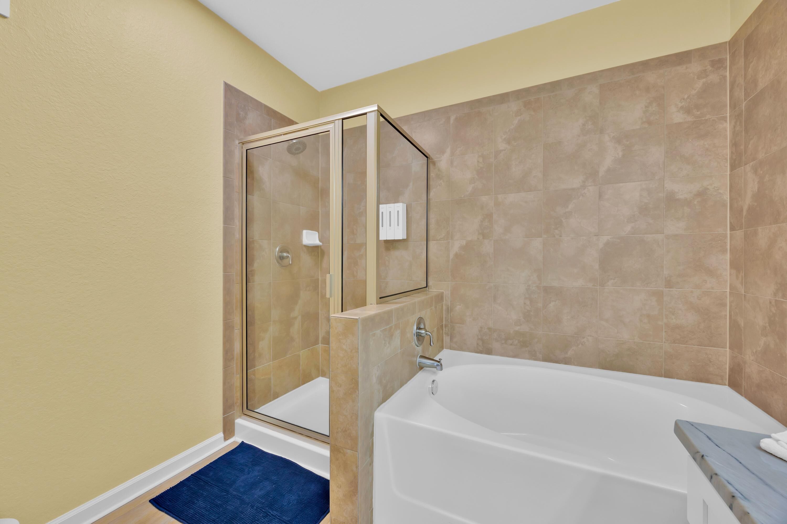 A bathroom with a glass shower enclosure, a bathtub, and beige tiled walls.