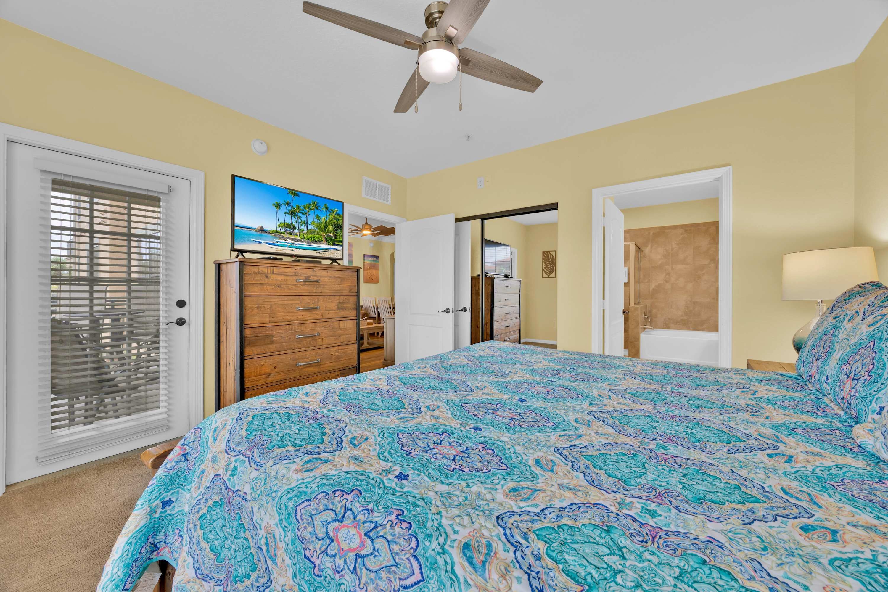 A bedroom with a bed, a ceiling fan, a dresser, a TV, and a door leading to another room.