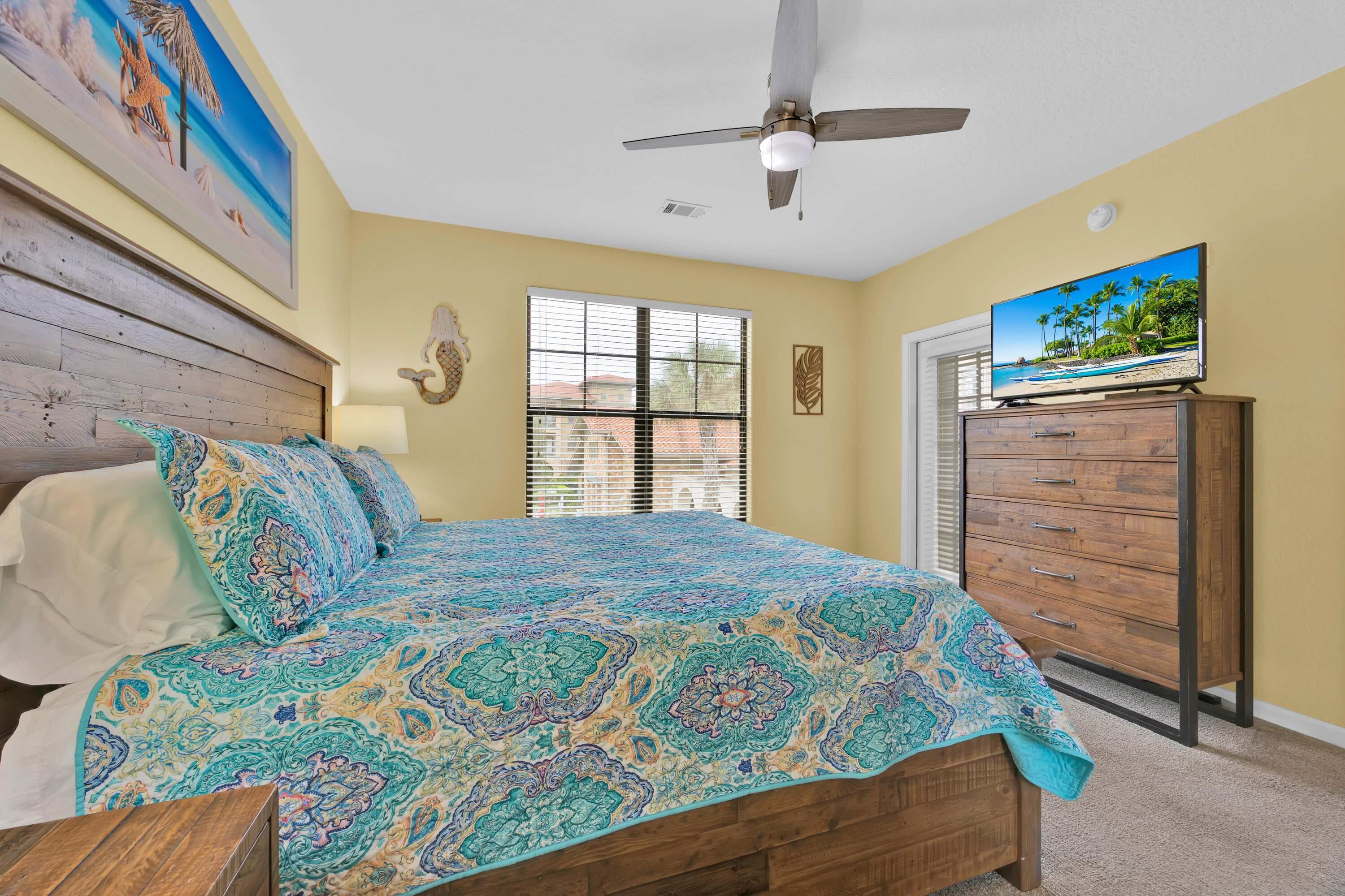 A bedroom with a bed, a ceiling fan, a dresser, a television, and a window with blinds.