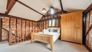 A bedroom with exposed brick walls, a wooden bed, a large wardrobe, and a sloped ceiling with wooden beams.