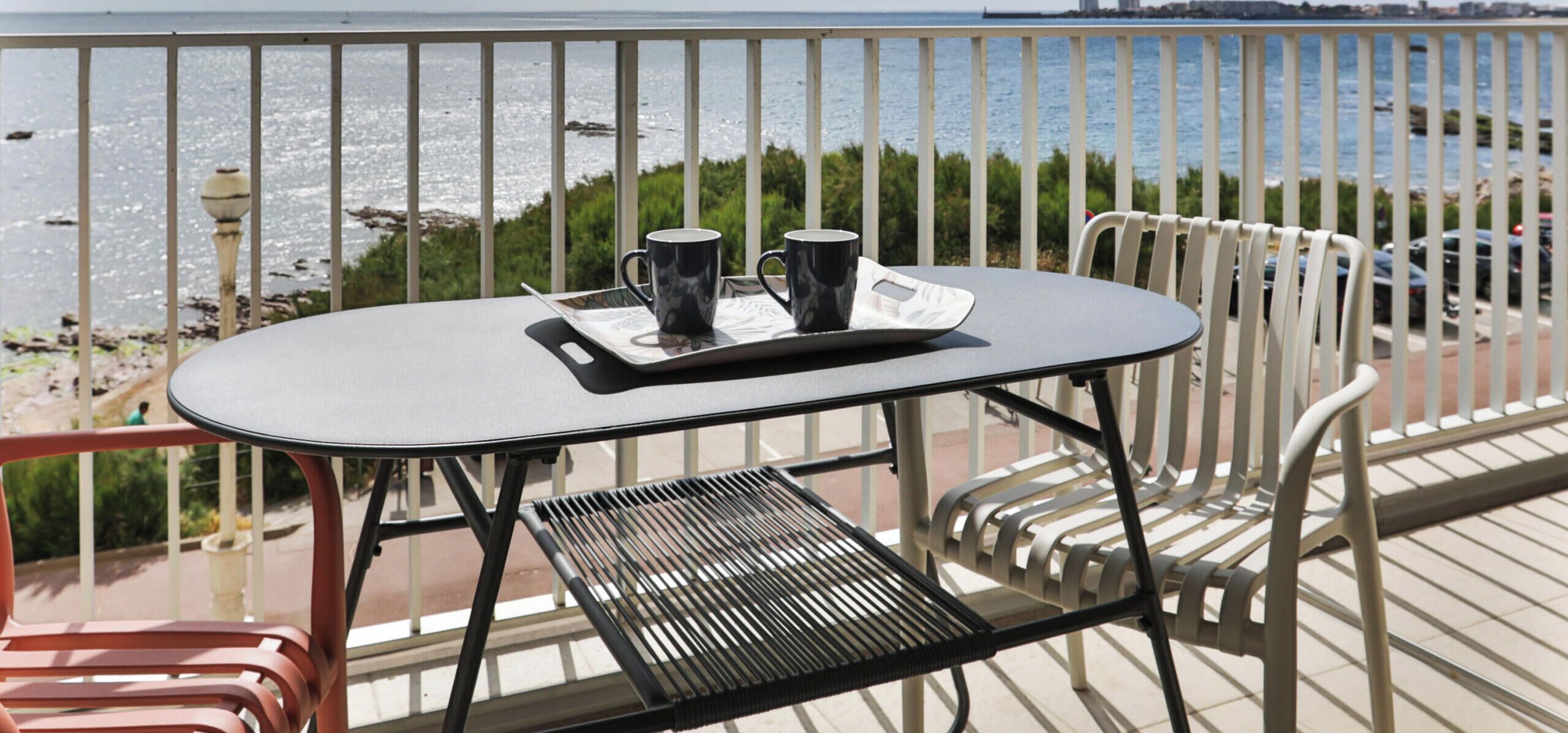 En balkon med et bord, to stole og to krus på et bakke.
