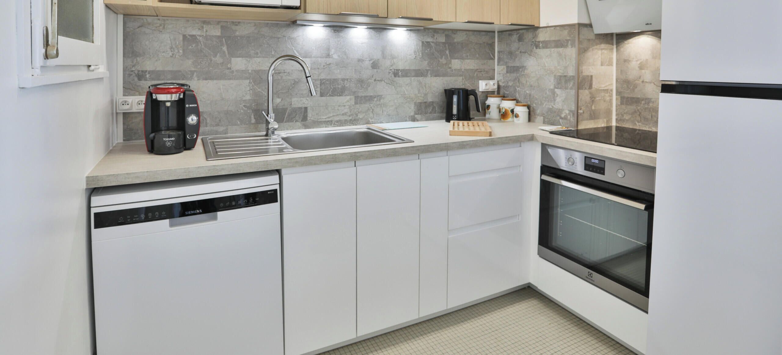 A modern kitchen with a dishwasher, a coffee maker, a sink, and an oven.