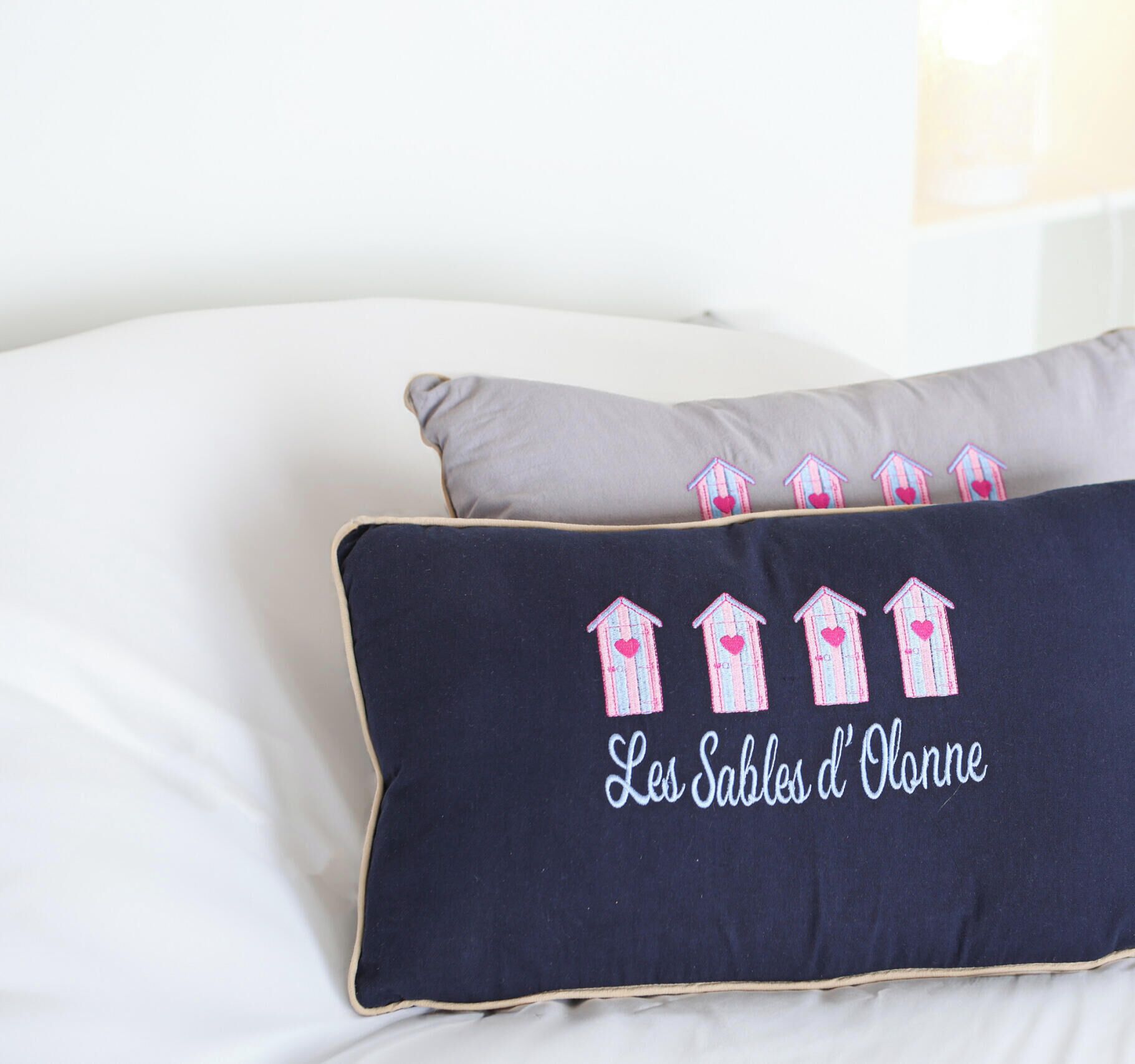 A bed with two pillows, one grey and one dark blue with embroidered houses and text.