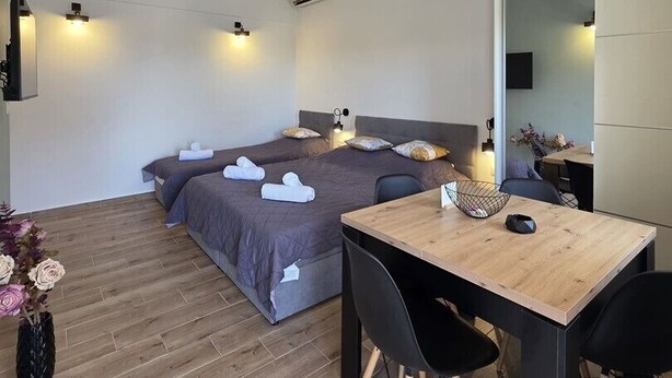 Een moderne hotelkamer met twee bedden, een houten eettafel, zwarte stoelen en een klein bijzettafeltje.