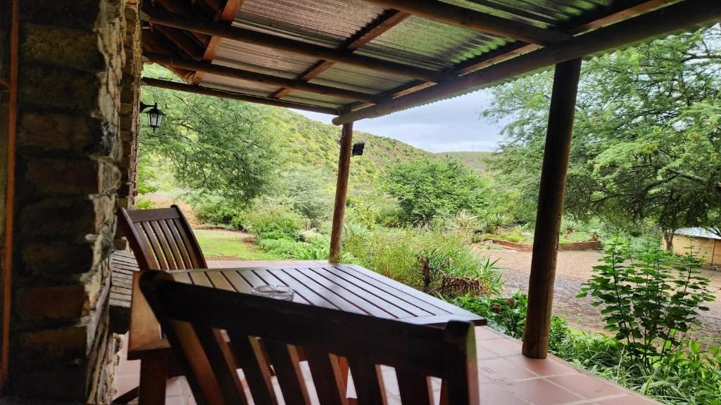 A covered outdoor seating area with a table and chairs, overlooking a lush garden and hilly landscape.