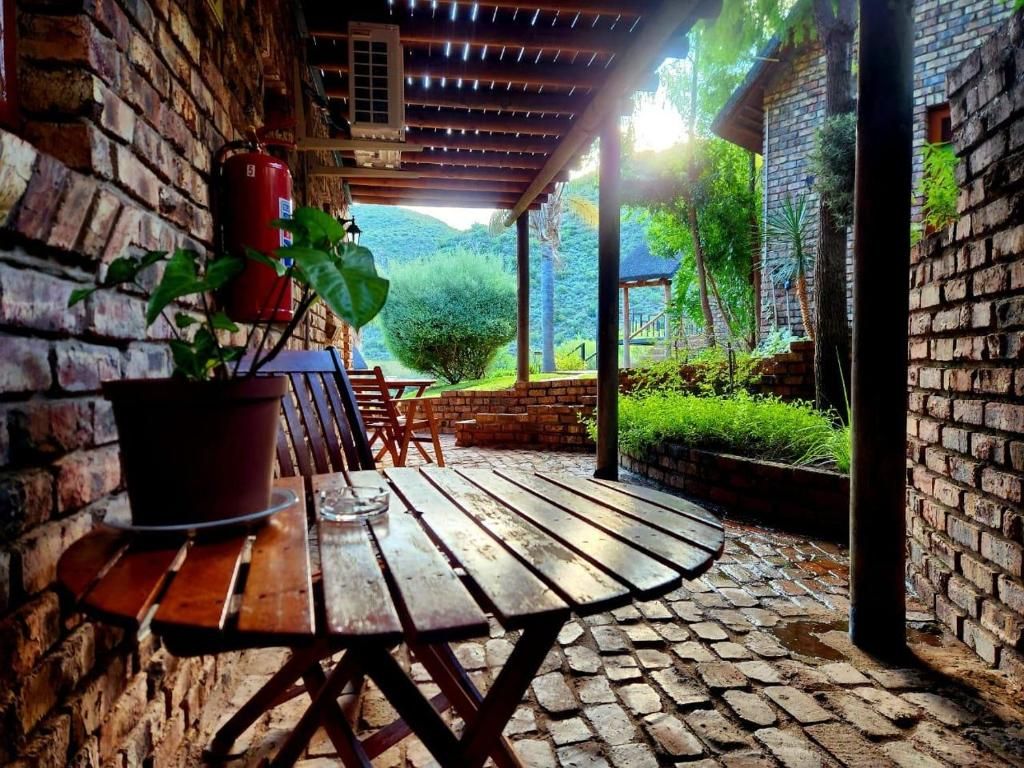 A covered patio with a wooden table and chairs, surrounded by brick walls and greenery.