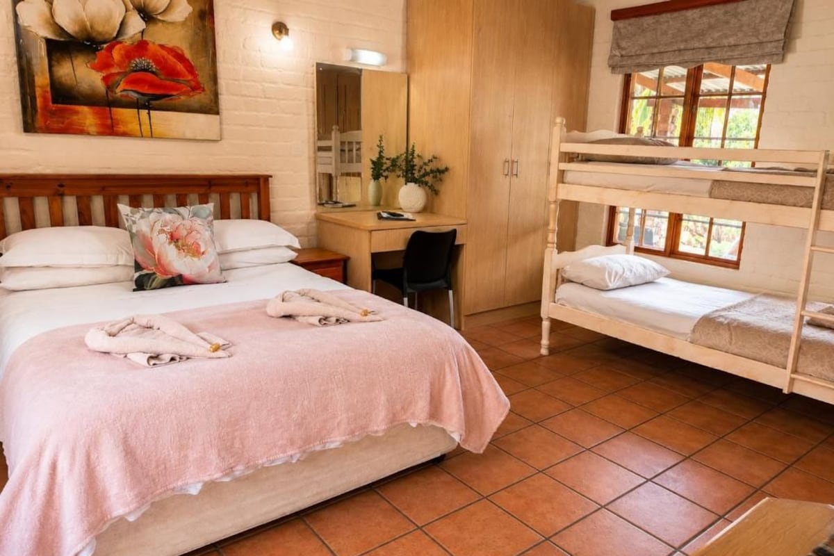 Ein Schlafzimmer mit einem großen Bett, einem Schreibtisch, einem Computer, einem Etagenbett und einem Gemälde an der Wand.