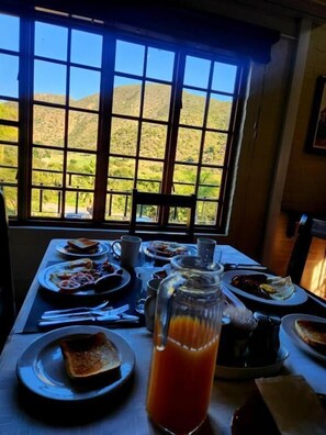 Ein Esstisch mit Speisen, ein Saftkrug und Blick auf Berge durch ein Fenster.