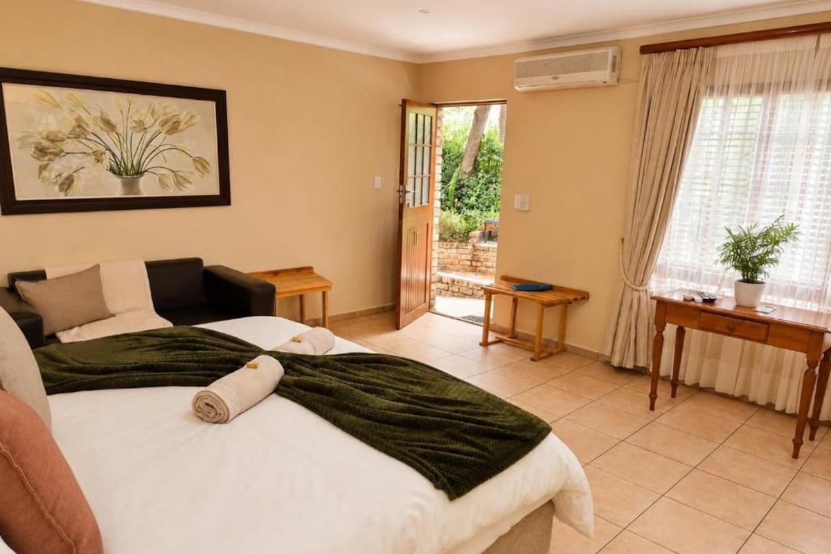Ein Hotelzimmer mit Bett, Schreibtisch, Stuhl, einem fenster mit Vorhängen und einer Tür zu einem Außenbereich.