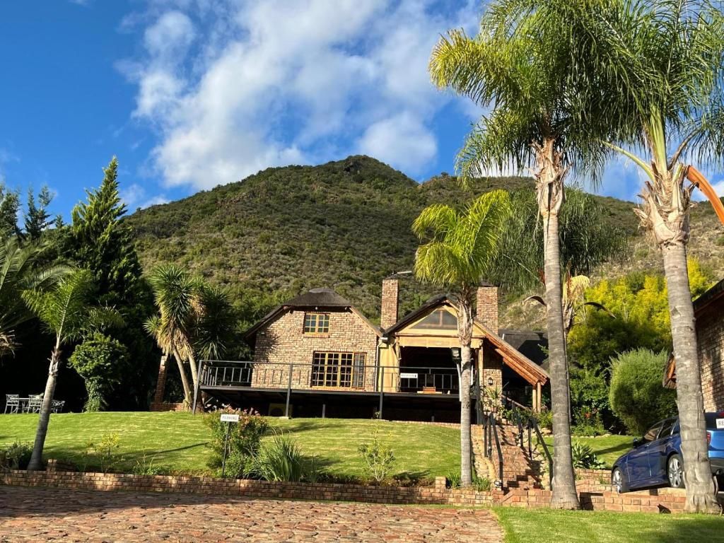 A stone house with a balcony, surrounded by a well-maintained lawn and palm trees, with a mountain in the background.