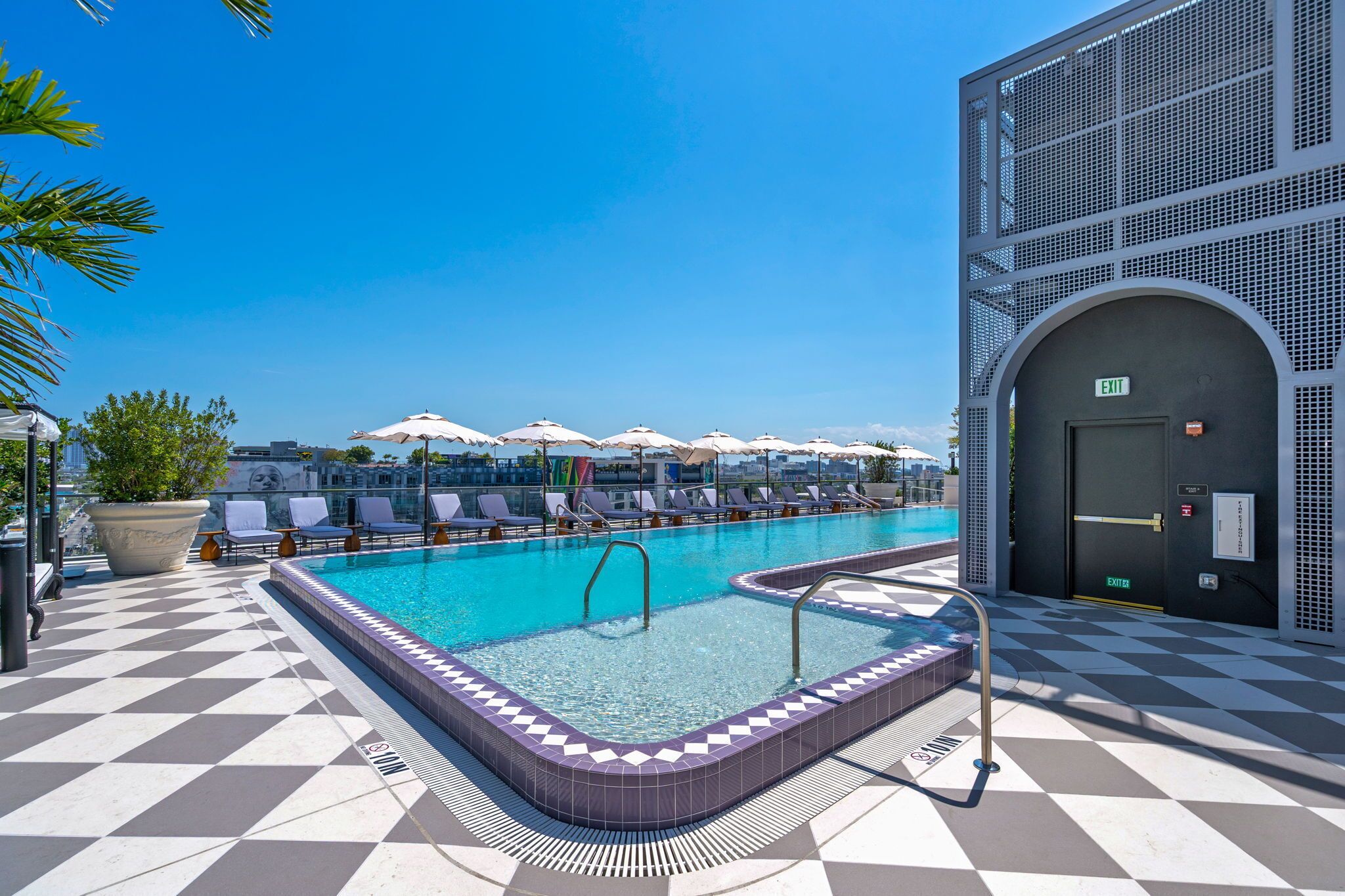 Piscina no terraço com piso quadriculado, cadeiras de descanso, guarda-sóis e céu azul.