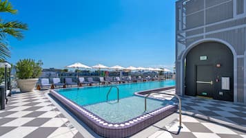 Piscina no terraço com piso quadriculado, cadeiras de descanso, guarda-sóis e céu azul.