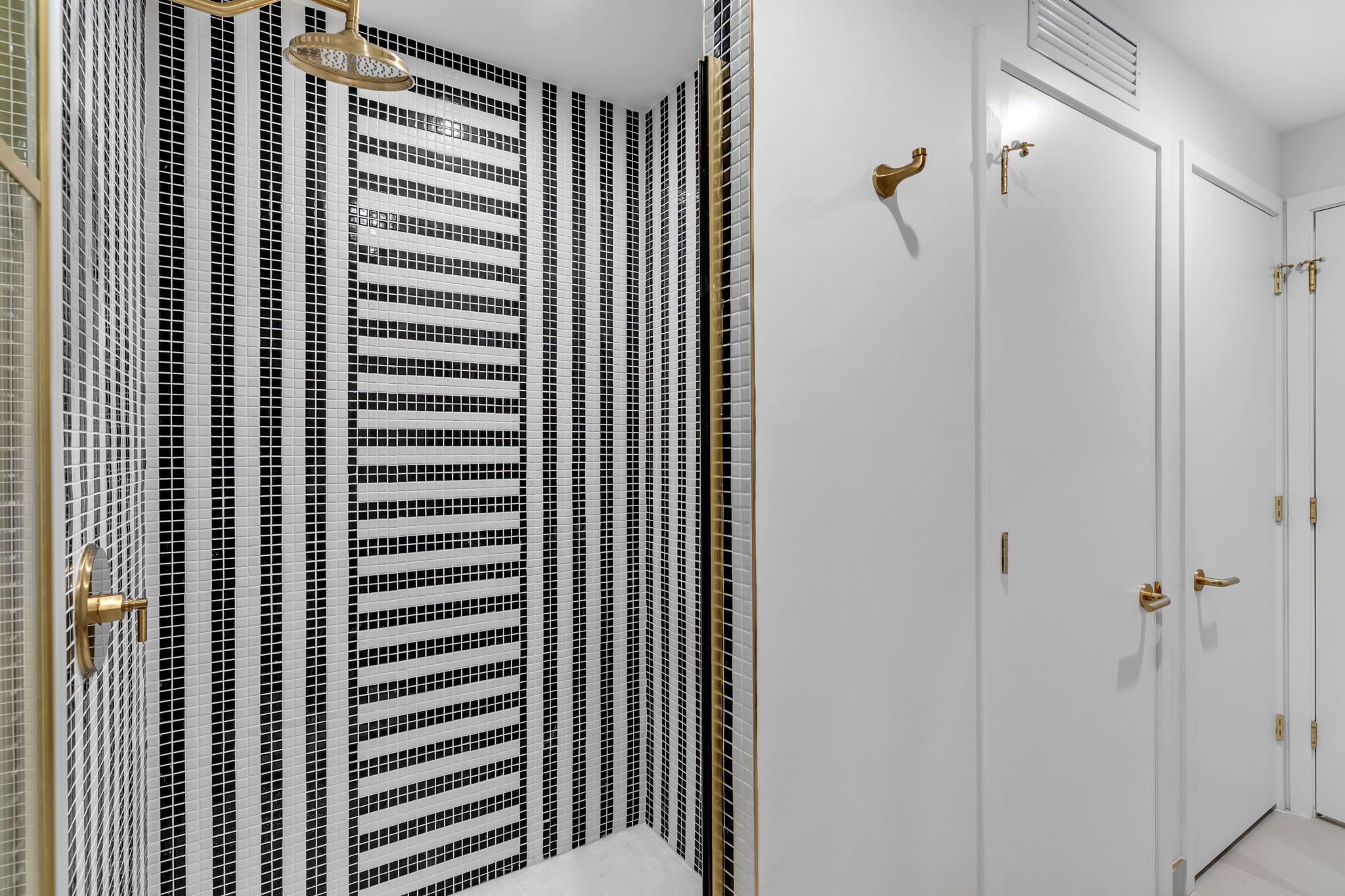 Een badkamer met een wand betegeld in zwart en wit strepen, een gouden douchekop en een witte deur met gouden handgrepen.