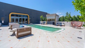 Zona de piscina amb gandules, banyera hidromassatge i edifici amb entrada de vidre.