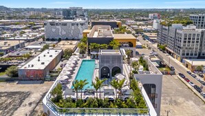 Una piscina a la terrassa amb gandules i ombrelles, envoltada d'edificis i vegetació.