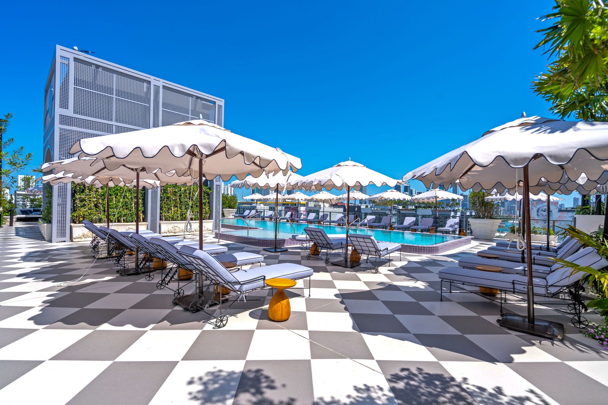 A rooftop pool area with sun loungers, umbrellas, and a checkered floor.