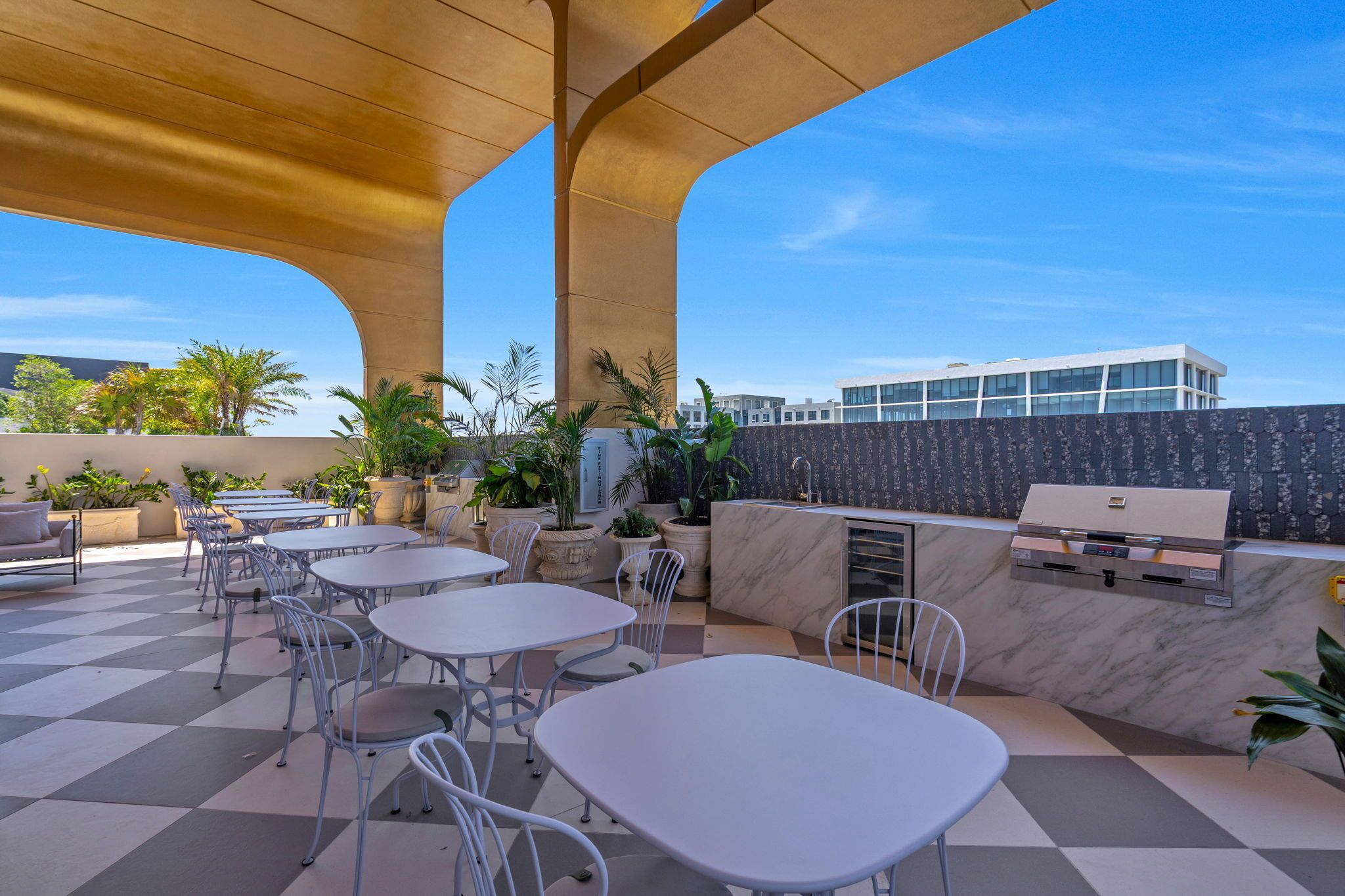 An outdoor patio with tables and chairs, a grill, and potted plants.