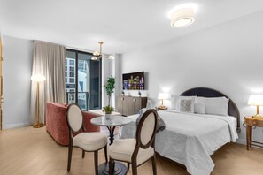 Ein Hotelzimmer mit Bett, Nachttischen, einem Schreibtisch mit Stuhl, einem roten Sofa, einer Topfpflanze und Blick auf die Stadt.