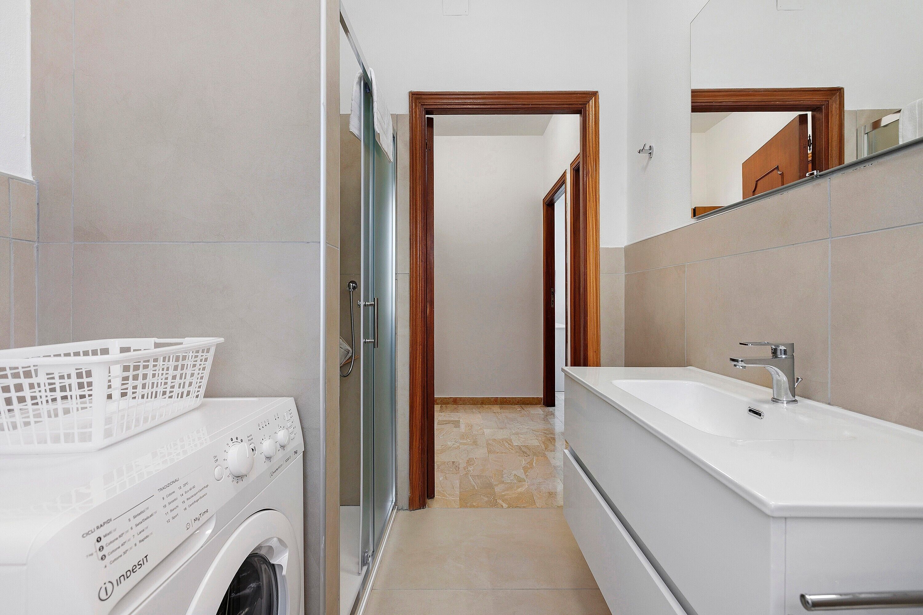 A laundry room with a washing machine, a sink, and a mirror.