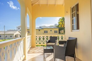 Ein Balkon mit Korbmöbeln, einem weißen Geländer und Blick auf Gebäude im Hintergrund.