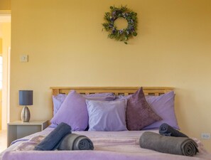 Ein Bett mit violetter Bettwäsche, einem Holz-Kopfschild und einem Wandkranz.