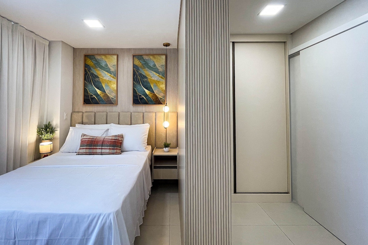 Ein Hotelzimmer mit Bett, zwei an der Wand befestigten Bildern, einem Nachttisch mit Lampe und einer Tür.