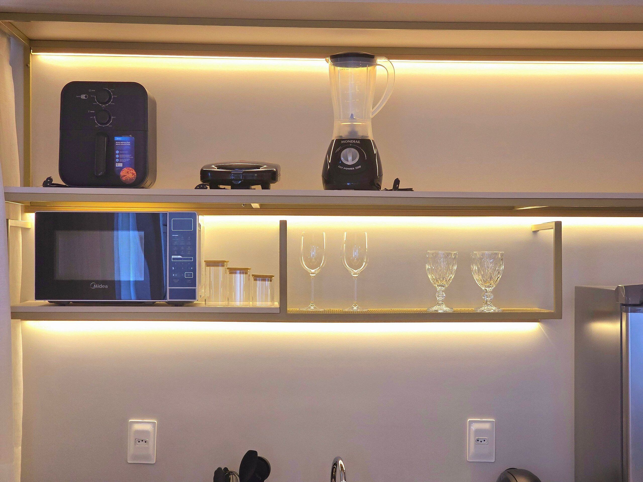 A kitchen with a microwave, blender, and wine glasses on shelves.