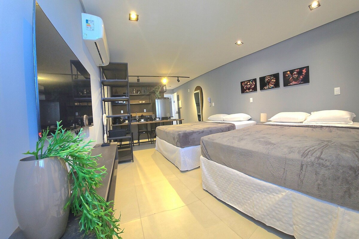 Ein Hotelzimmer mit Bett, Schreibtisch, Stuhl, Pflanze und Fernseher.