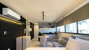 A modern hotel room with a bed, a sofa, a small kitchen area, and a large window offering a city view. - Voll29 by Hosppedar (João Pessoa)