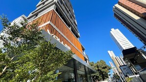 A modern high-rise building with a unique wooden facade, surrounded by other tall buildings and clear blue sky. - Voll29 by Hosppedar (João Pessoa)
