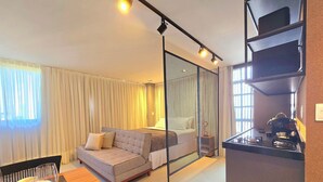 A modern living room with a sofa, dining table, and kitchen area with a coffee machine. - Voll29 by Hosppedar (João Pessoa)