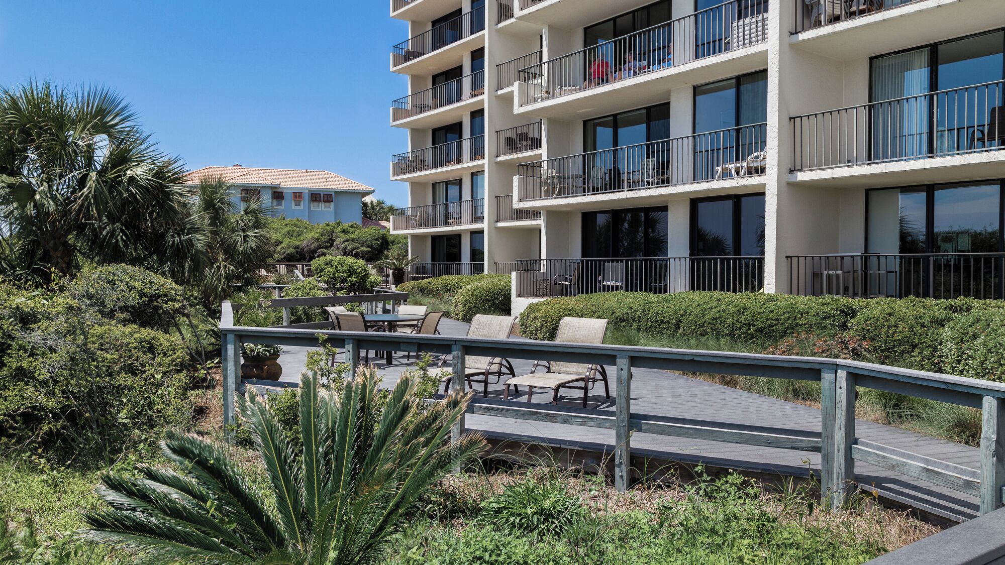 A multi-story hotel with outdoor seating, a wooden deck, and a clear view of the surrounding greenery.