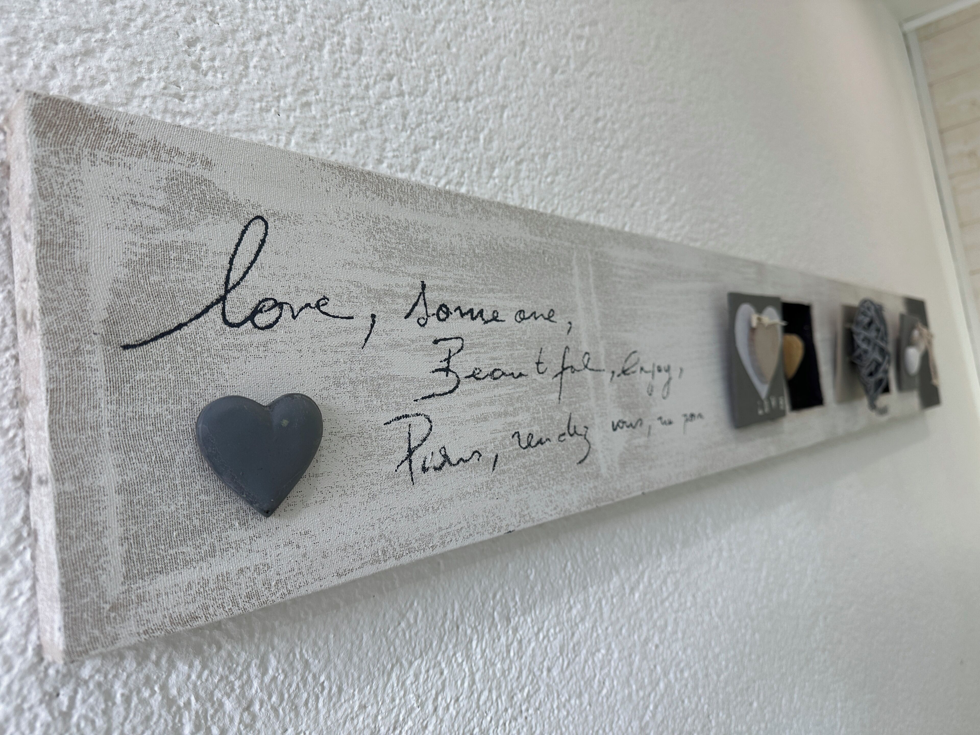 A textured wall with a mounted piece of art featuring handwritten text and a heart.