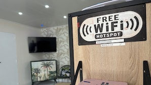 Habitació amb un senyal que indica punt d'accés WiFi gratuït, televisió de pantalla plana penjada a la paret i taula petita amb un dispositiu blanc a sobre.