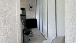 Un interior modern i minimalista, amb una paret blanca amb textura, una cadira blanca i una cuina al fons.