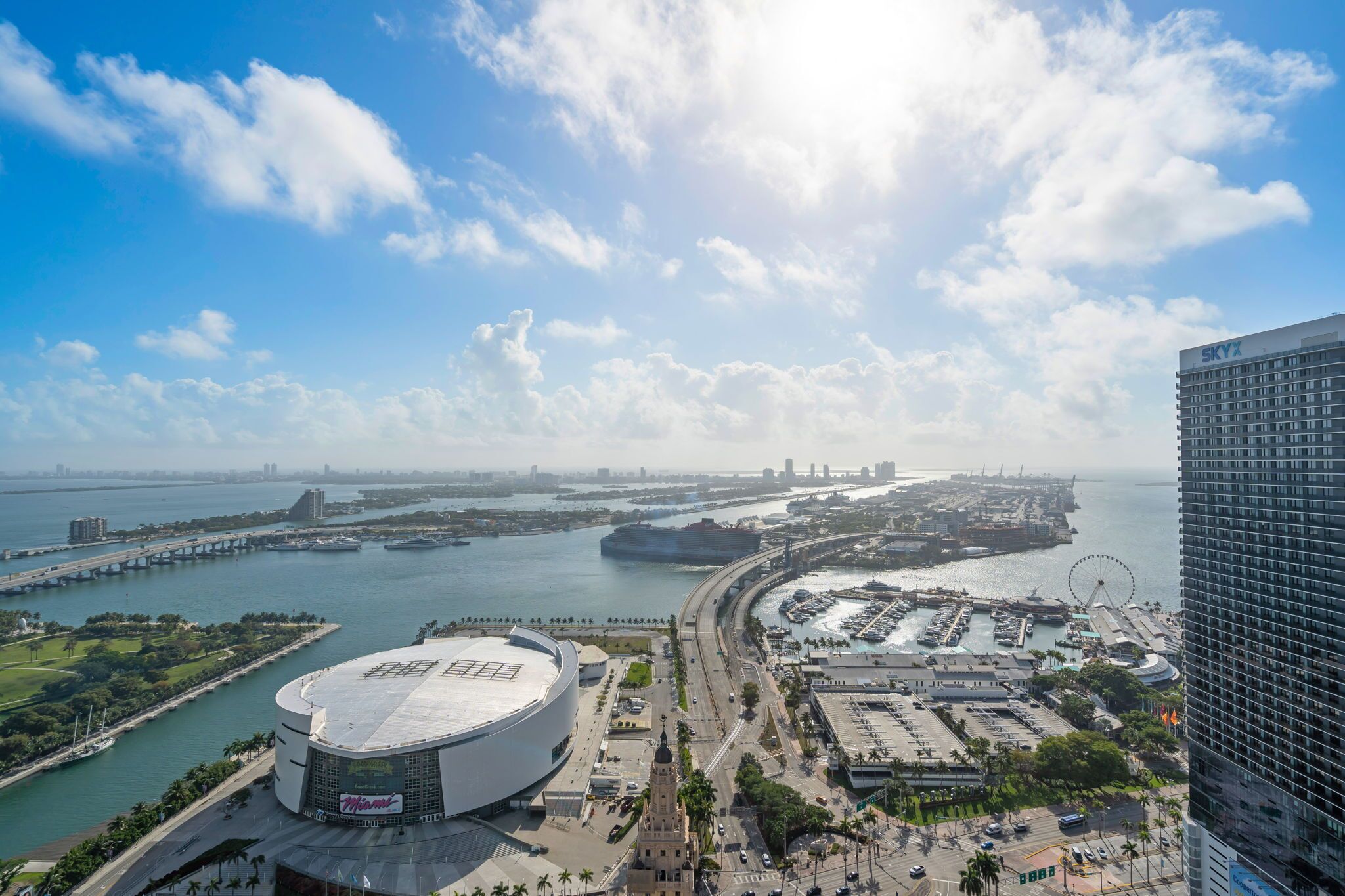 A waterfront view with a large stadium, a Ferris wheel, and a modern hotel.