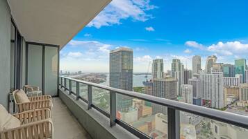 A balcony with a city view, a railing, and two wicker chairs.