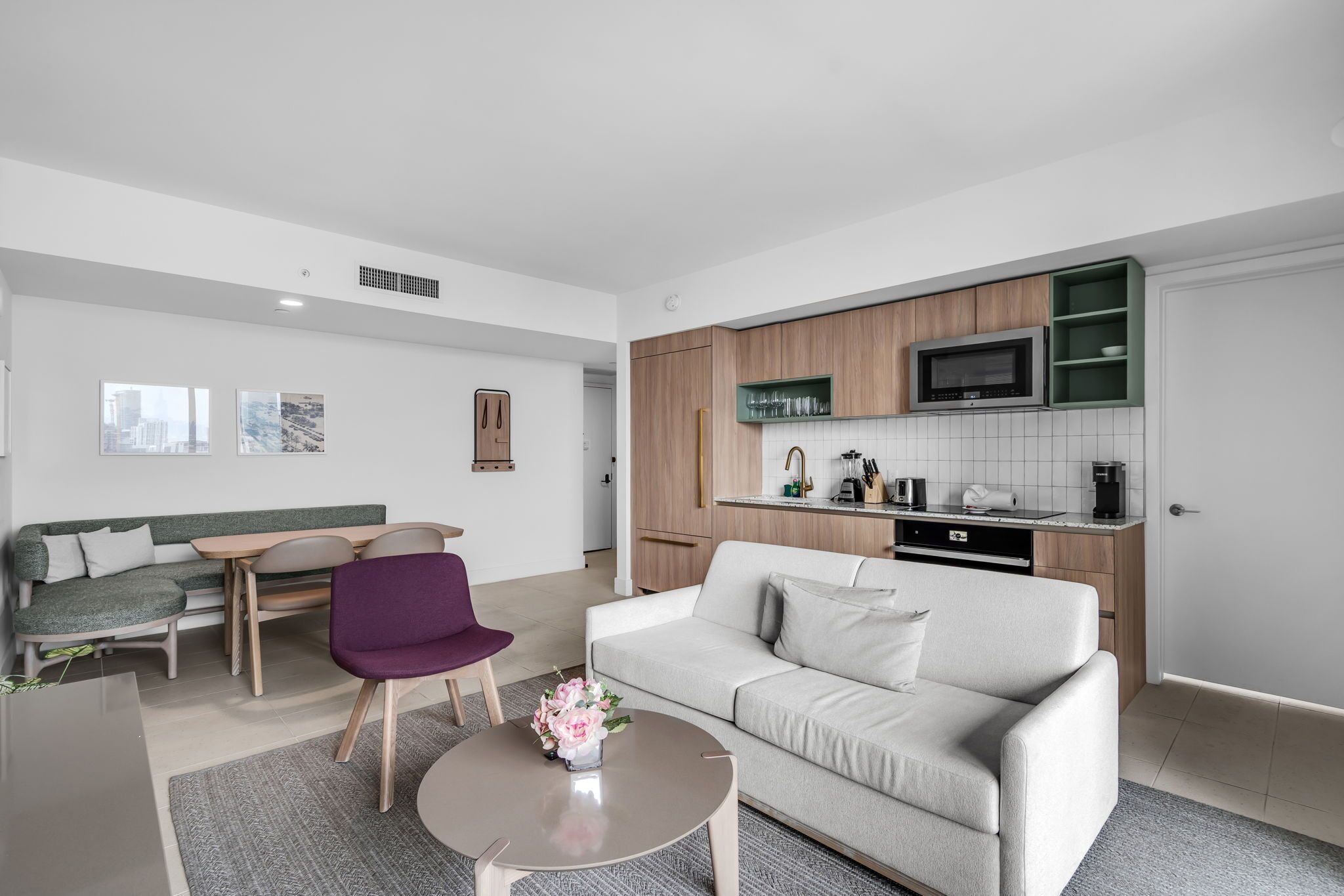 A modern living room with a sofa, chairs, a coffee table, and a kitchen area with cabinets and appliances.