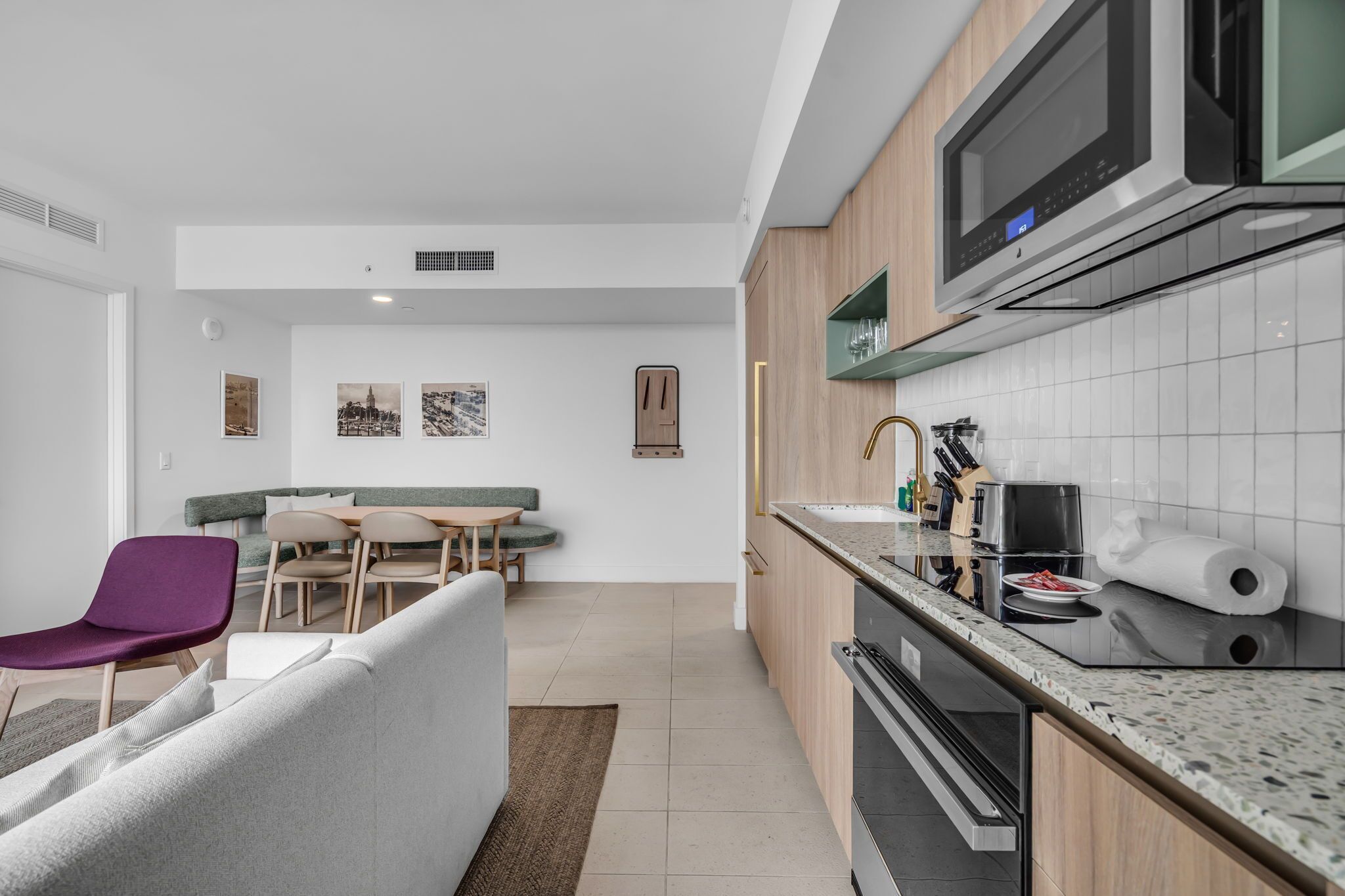 Una cocina moderna con microondas integrado, un comedor con sofá verde y una zona de estar con una silla morada.