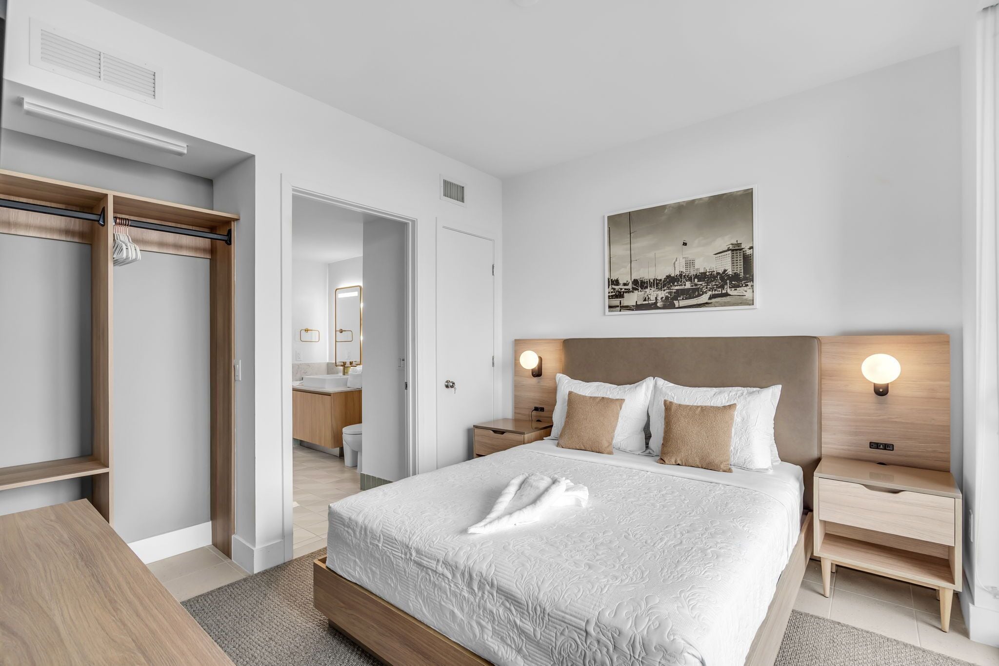 Une chambre d’hôtel comprenant un lit, des tables de chevet, une armoire, une salle de bain et un tableau représentant un paysage urbain.