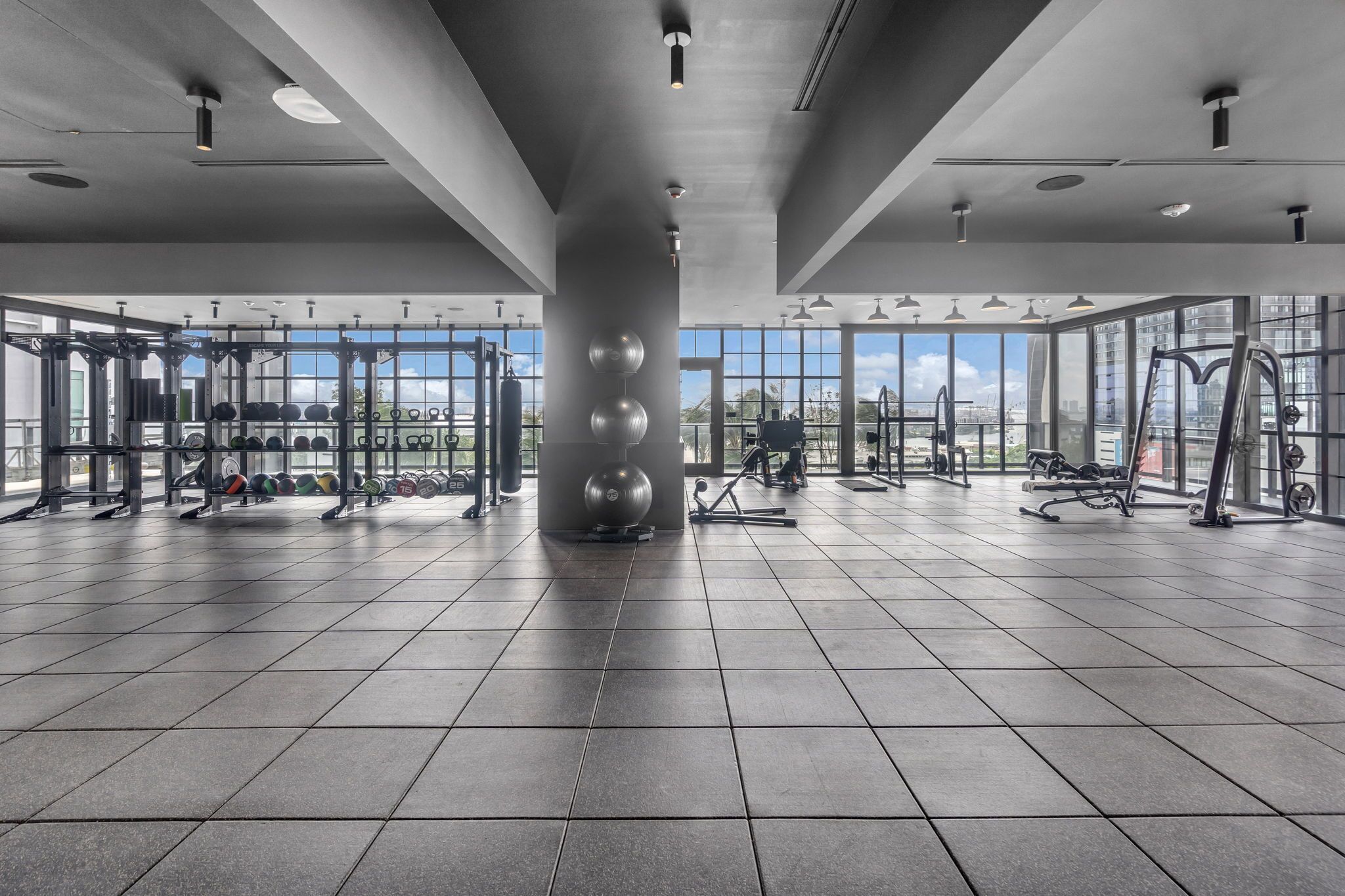 Un gimnasio amplio con ventanas grandes, equipo de levantamiento de pesas y un diseño moderno y limpio.