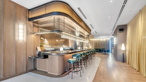 Uma área de bar moderna com balcão curvo, banquetas e um espaço de estar com mesas e cadeiras.