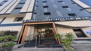 Un edificio moderno con fachada geométrica, una escalera que conduce a la entrada y un cartel que indica que es un complejo de apartamentos con servicios.