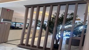Una partición de madera con listones verticales, una planta en maceta y una vista parcial de una habitación con una lámpara de techo.