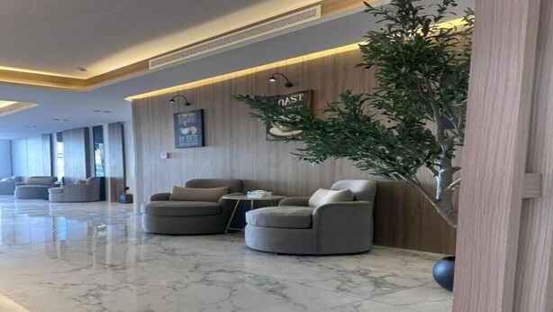 Un moderno vestíbulo con piso de mármol, zona de estar con sofás, una planta grande y una pared de madera con un letrero.