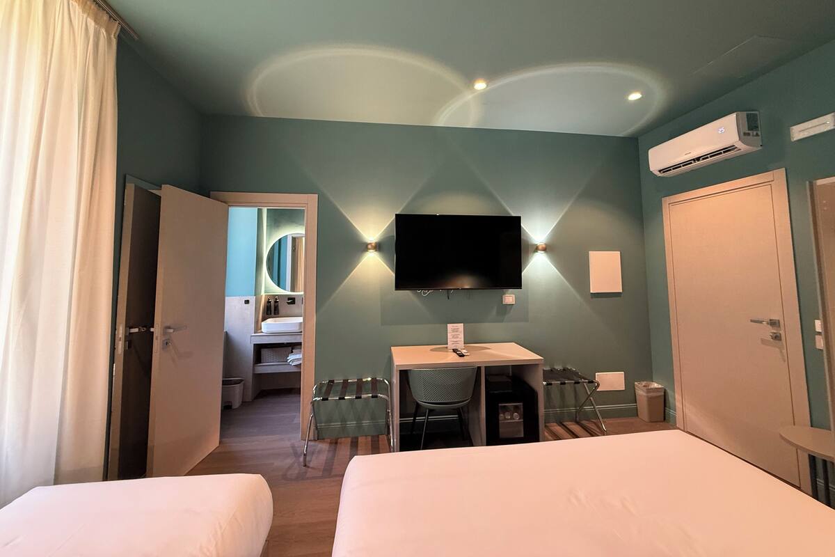 Et hotelværelse med to senge, et skrivebord med stol, et fjernsyn og en aircondition.