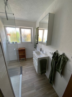 Un baño moderno con ducha, lavabo, espejo y ventana.