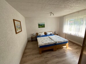 Un dormitorio con una cama doble, una mesita de noche, una lámpara, un cuadro enmarcado y una ventana con cortinas.