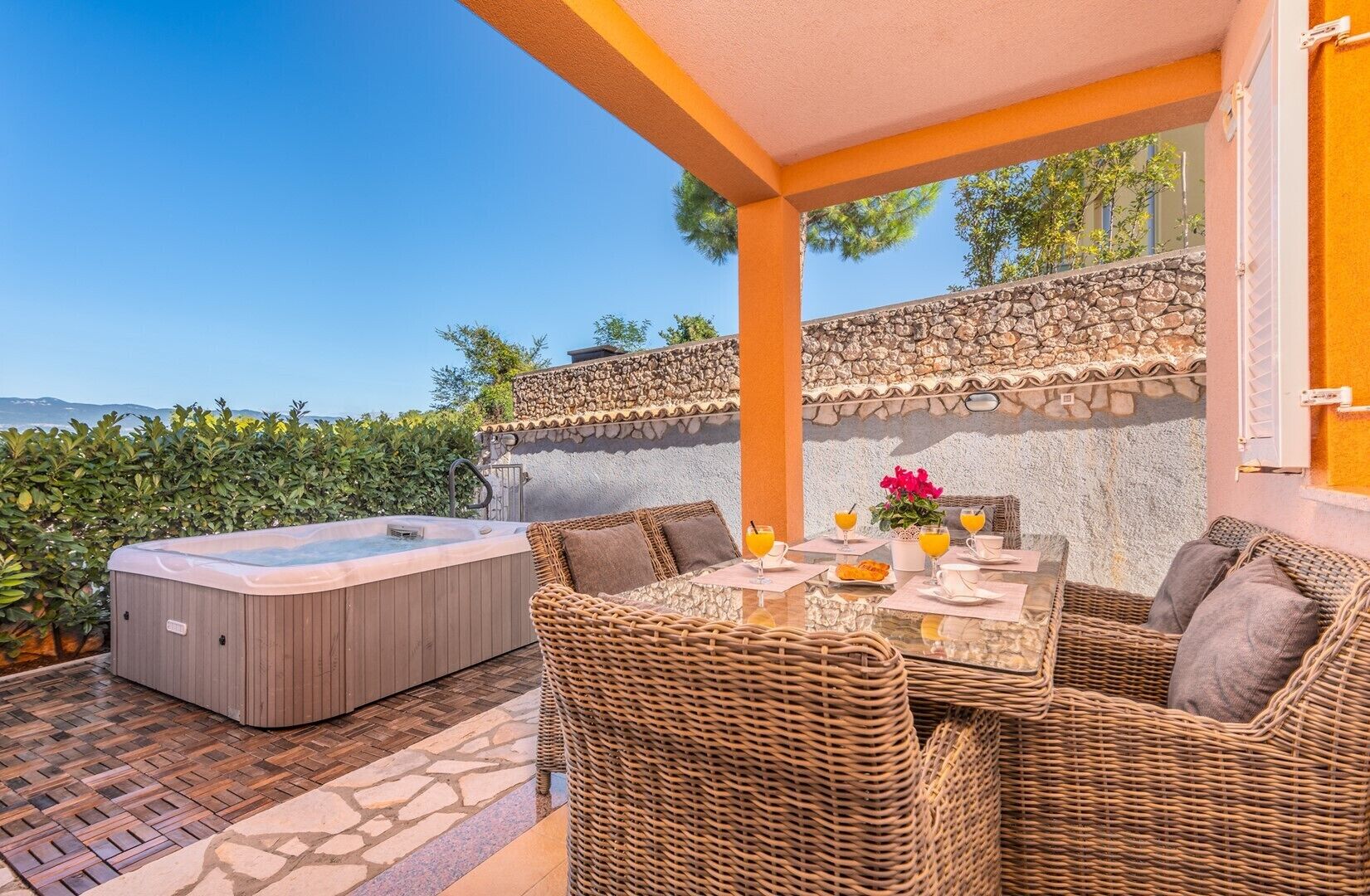 Een terras met een jacuzzi, rieten meubels en een tafel voor twee compleet met drankjes.