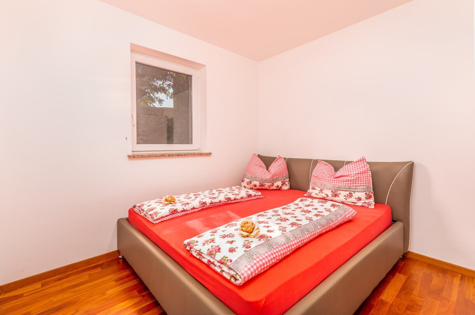 Un dormitorio con cama, ventana y suelo de madera.